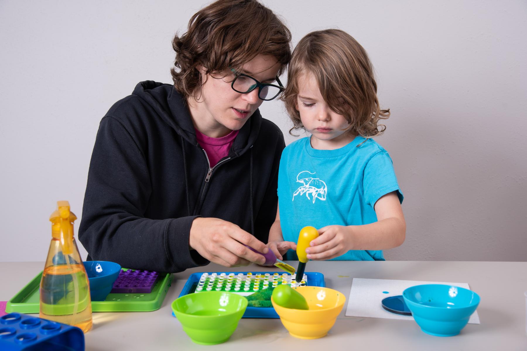 Facilitator and young learner squeeze colored water into a dish