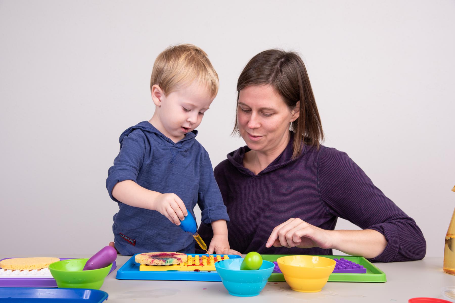 A young learner and a facilitator are experimenting squeezing colored water into a tray 