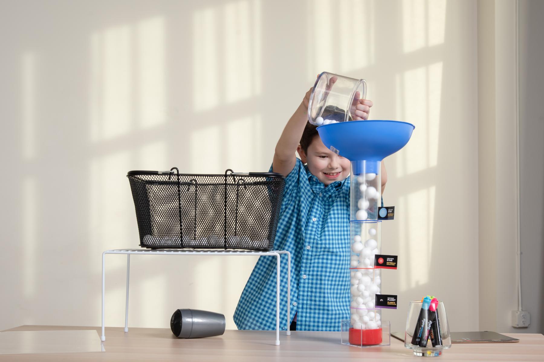 A young learner pours his collected styrofoam balls into a measuring container