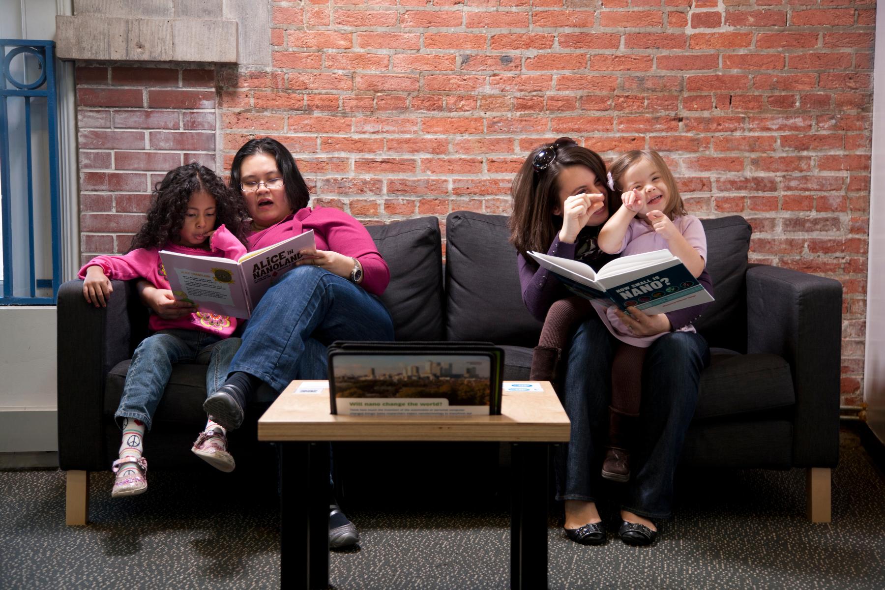 two mothers and children sitting on a couch reading Nano books in the Nano exhibition