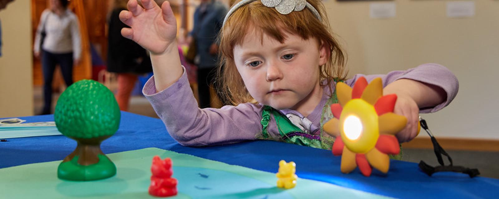 Young learner using a sun-shaped flashlight to make a shadow on small yellow and red toy bears