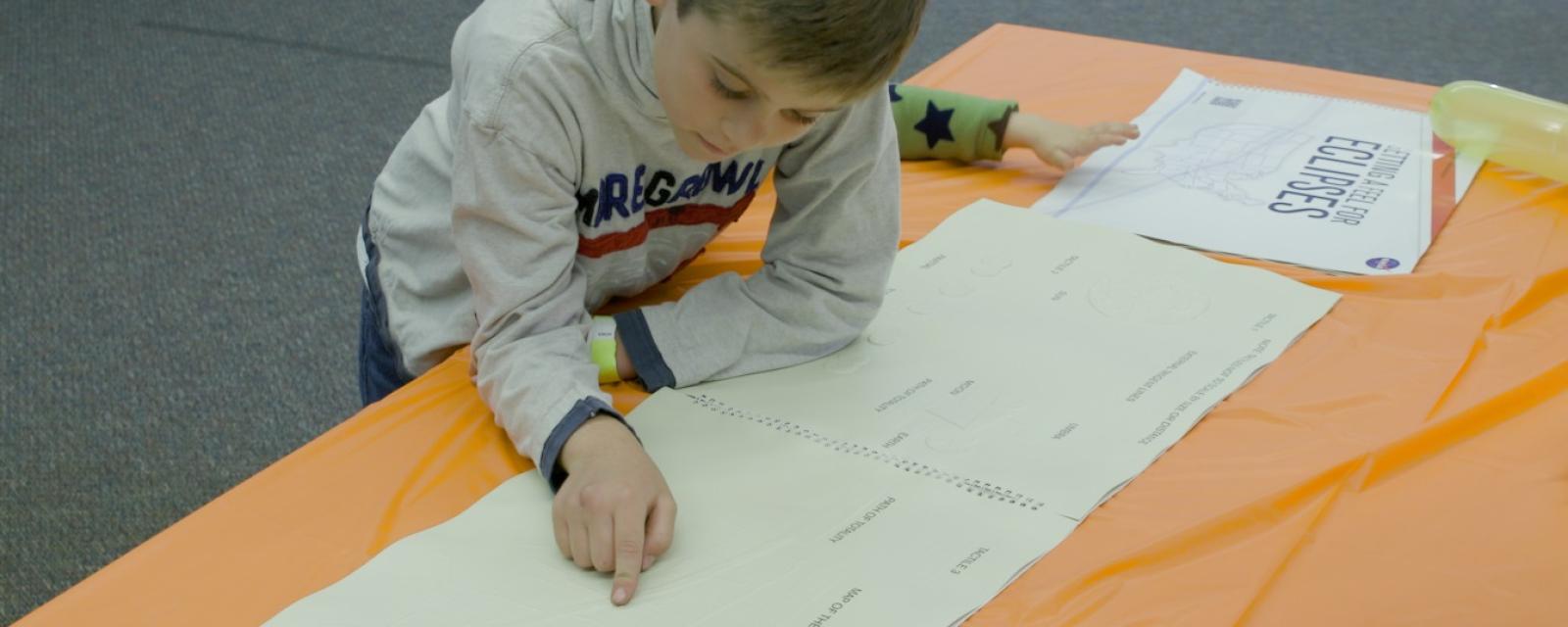 Child using the Braille book, called "Getting a Feel for Eclipses," features graphics that teach users about the interaction and alignment of the sun with the moon and Earth