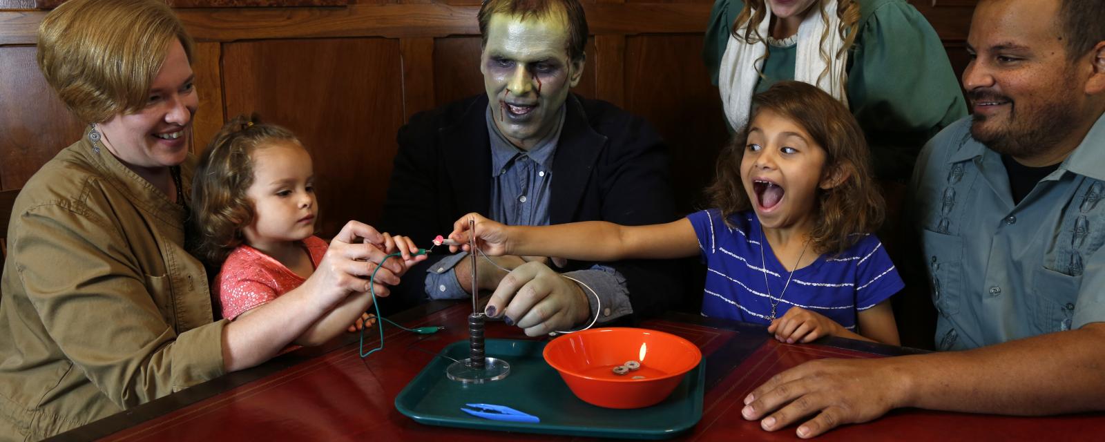 Children with surprised faces and adults using the Frankenstein kit Battery Stack activity - adults dressed as Mary Shelley and the Monster