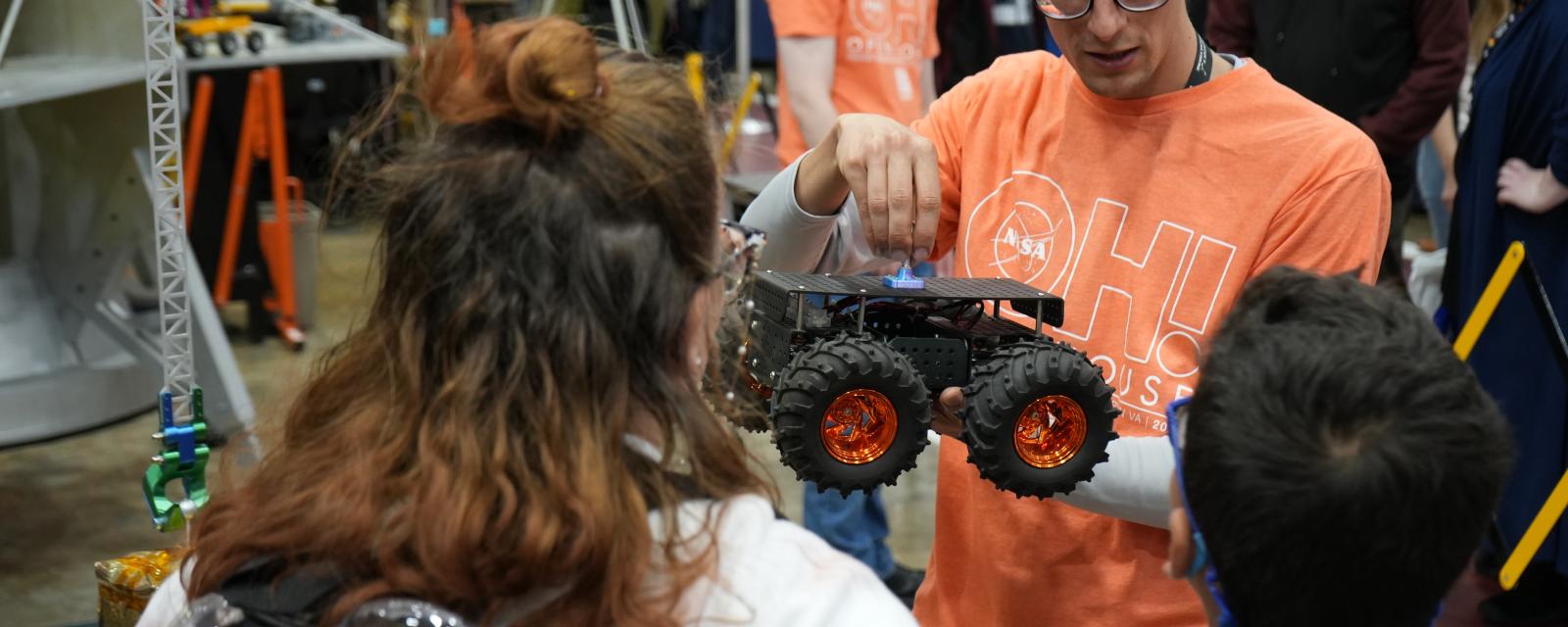 Educator Holds a Rover Model as Two Youth Listen and Learn More