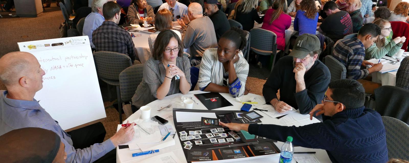 Museum of Science forums discussions featuring groups of people at tables writing on posters and discussing